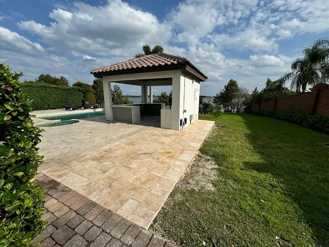 Travertine pool deck with a covered outdoor kitchen overlooking a lake